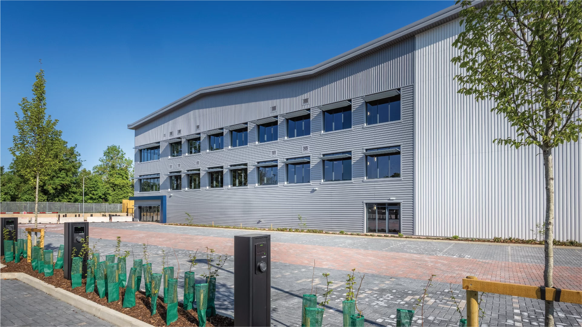Modern industrial building with trees and charging stations.